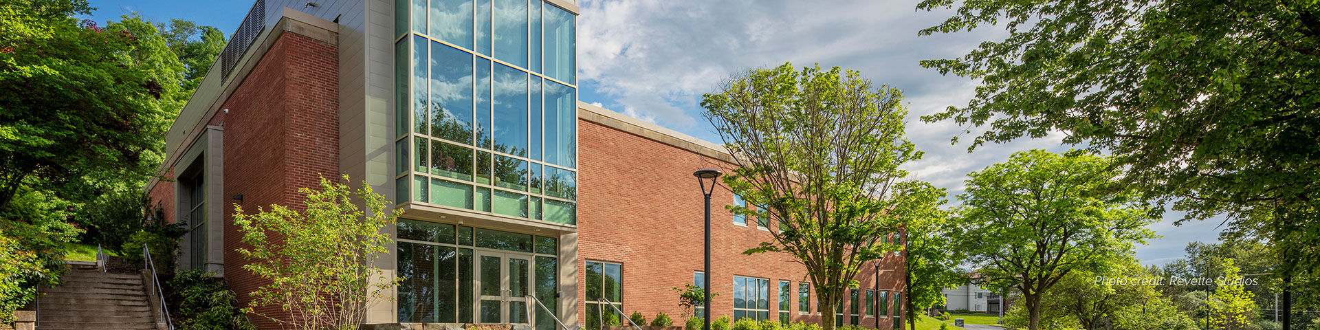 brick building with a modern looking glass foyer surrounded by green trees