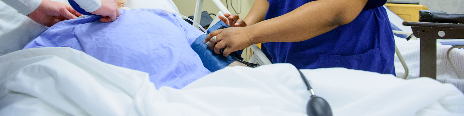 two nurses check vitals on a patient in a hospital bed