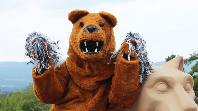 nitany lion mascot sitting next to lion shrine cheering with pompoms