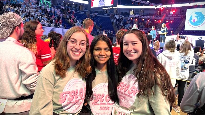 Three female students pose on the dance floor of the Bryce Jordan Center.