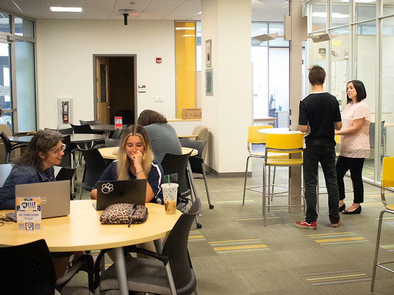 two students sitting at tables with an academic advisor looking at laptops 