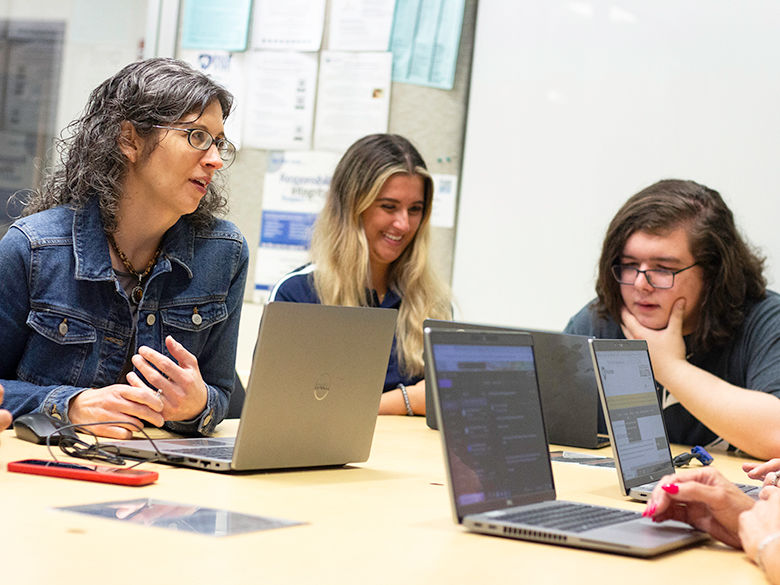 3 people at a conference room table reviewing their laptops