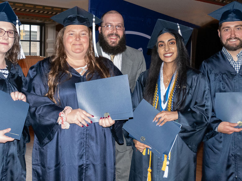 group of 5 diverse graduates in caps and gowns holding diplomas