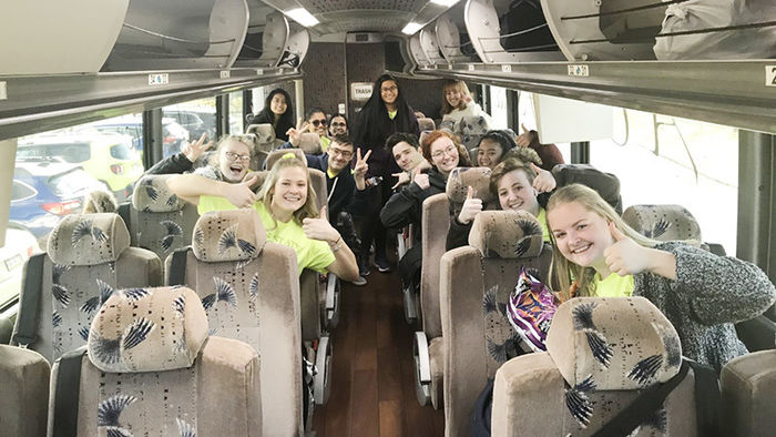 Students on a charter bus wave and hold up peace signs.