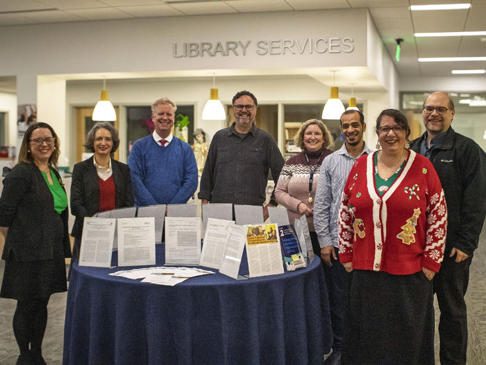 published faculty authors pose for a photo in the campus library near a display of their works