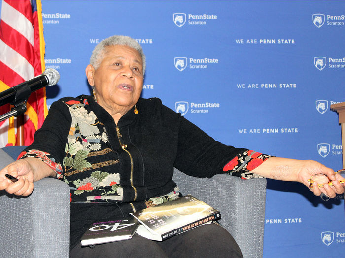 Minniejean Brown Trickey seated onstage in a chair, speaks to the crowd