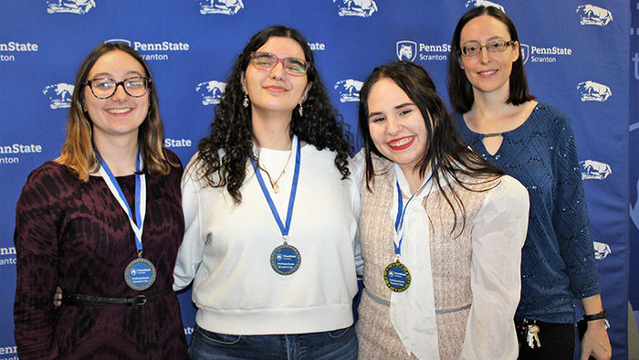 3 smiling women wearing medals pose with a teacher