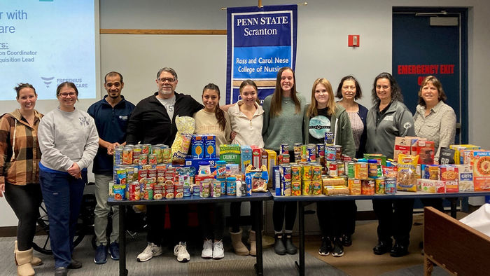 eleven people stand behind table stacked with canned goods