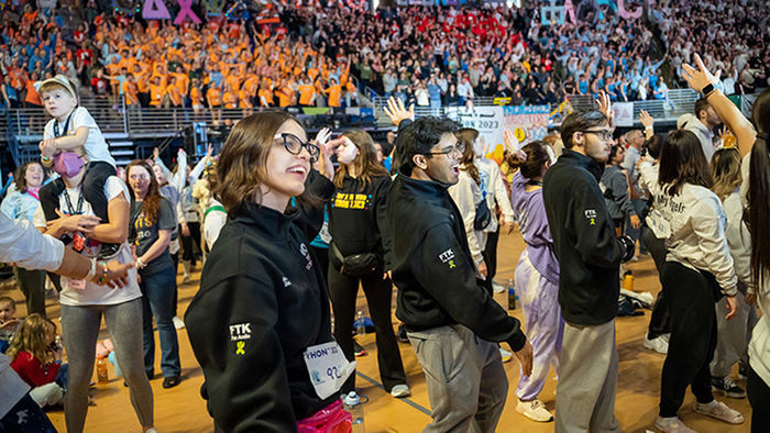 three smiling students dance in a crowded stadium