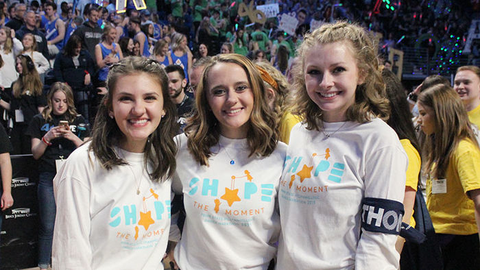 three students in front of large stadium crowd