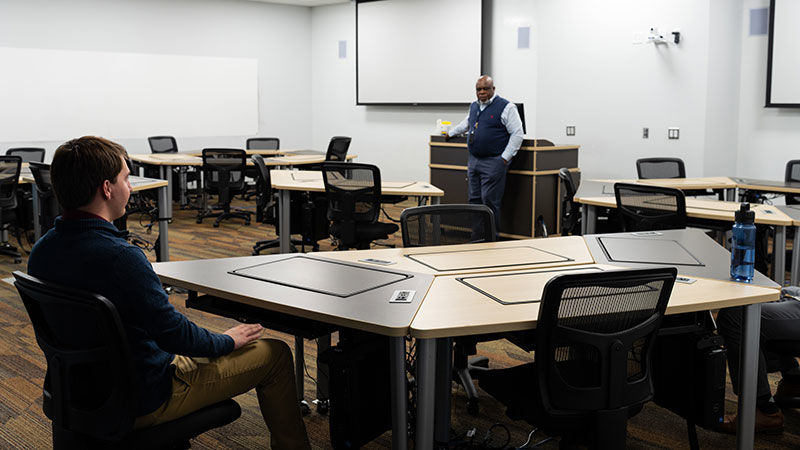 a student and teacher chat together in a large computer lab