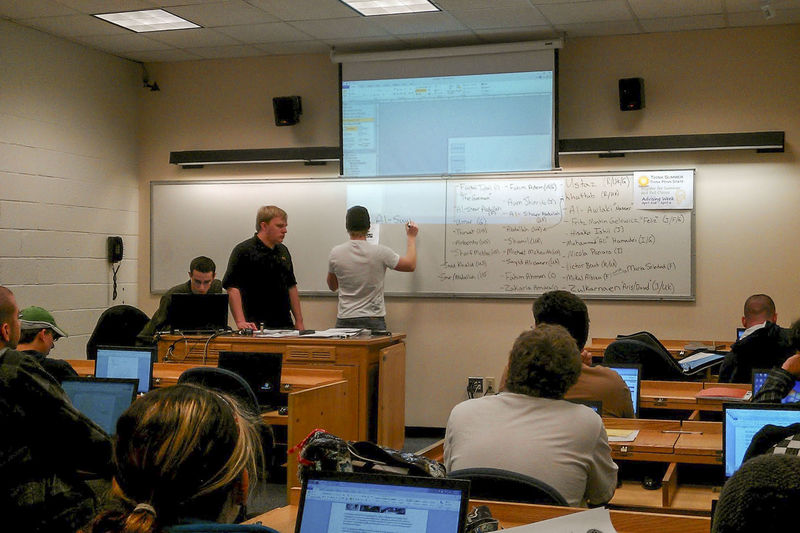 Students stand at a classroom whiteboard as other students watch