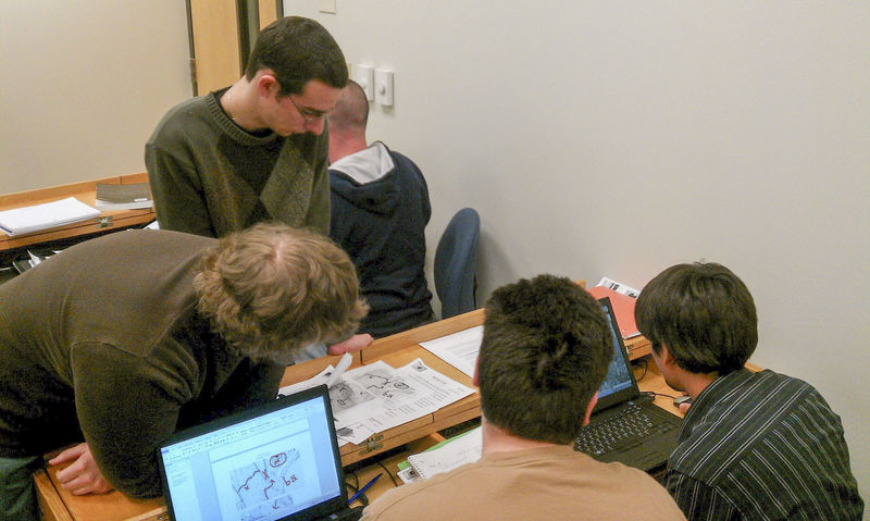 Students sit together while working at a computer on a desk