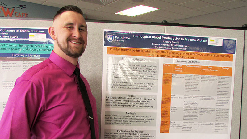 student standing next to poster of research project