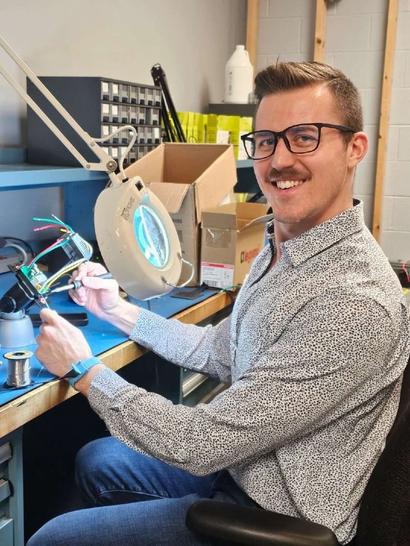 A student smiles for the camera while holding tools to work on a piece of computer hardware