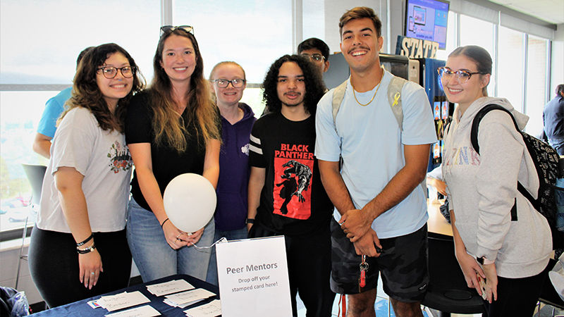 six students gather around peer mentor sign