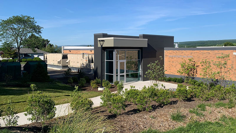 pathway lined with shrubs leads to modern glass entrance of one story brick building 