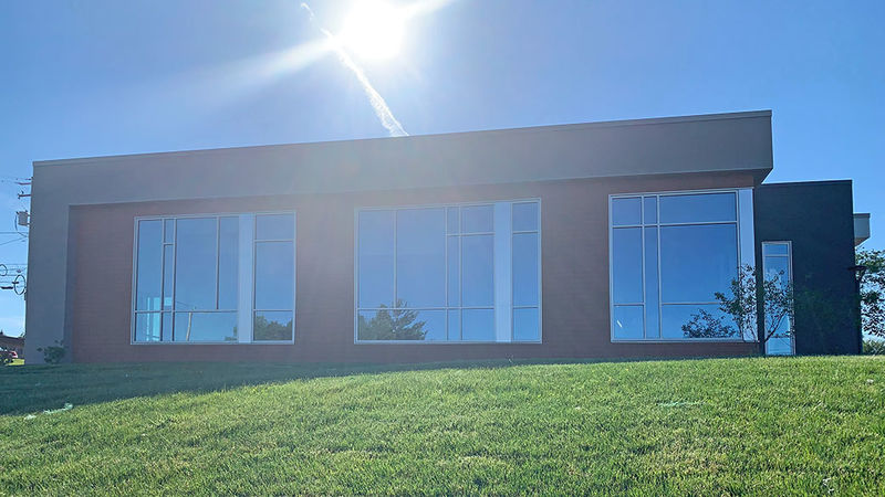 sign shining in blue sky over a one story brick building with large glass windows along the front