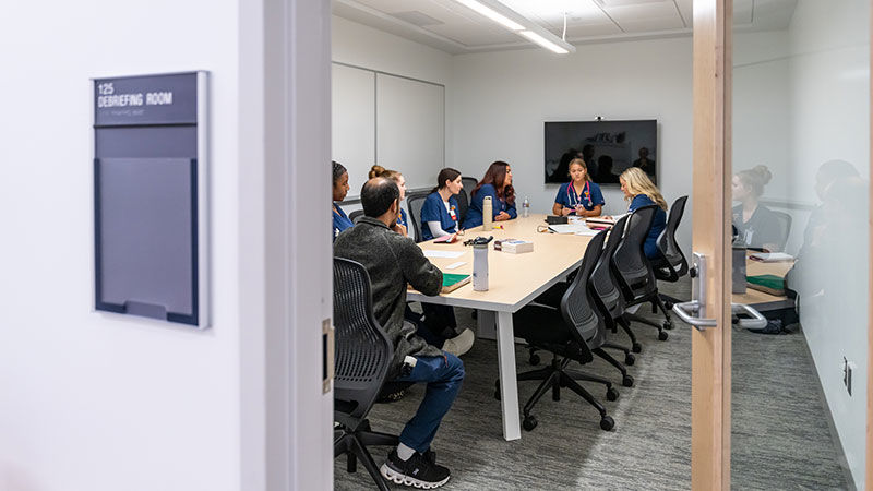 8 people in scrubs sit around a conference room table