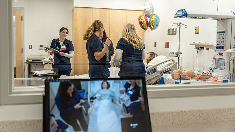 four students in scrubs attend to a pregnant mannequin in a lab that looks like a hospital room