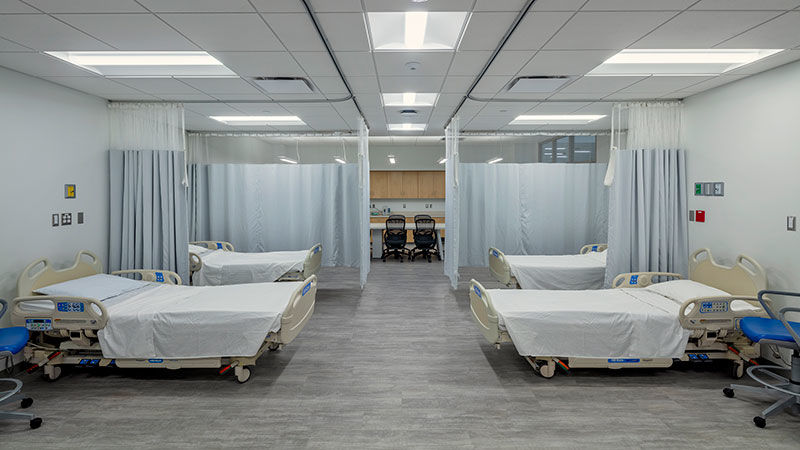 large brightly lit classroom with six hospital beds and privacy curtains, looks like a hospital setting