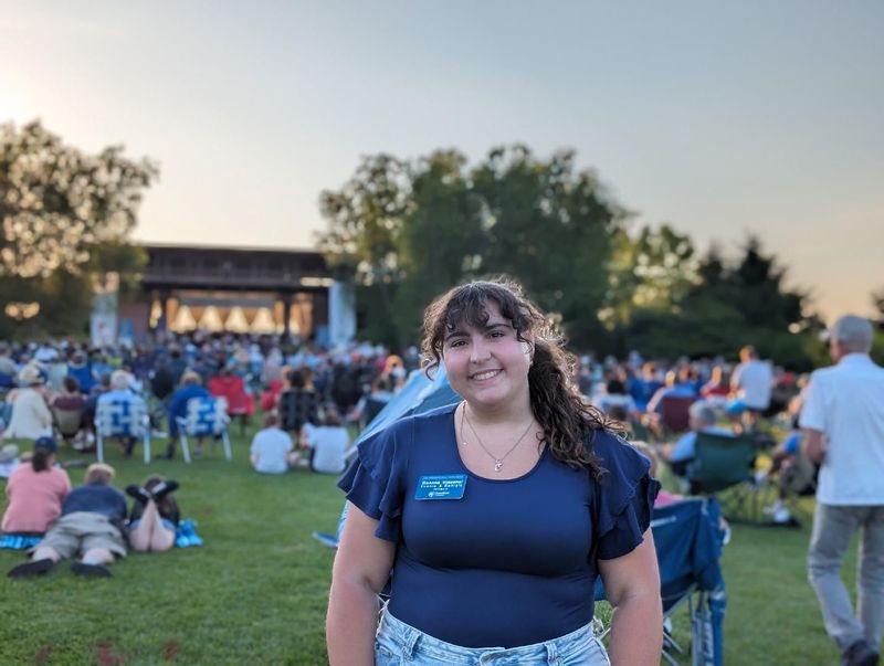 A student stands in the foreground of an outdoor event with a crowd