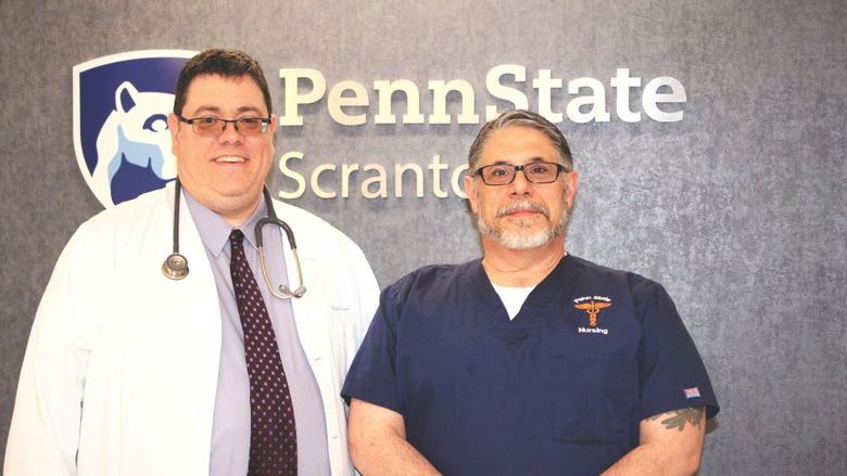 photo of Mike Evans and Frank Turnbaugh standing in front of wall with Penn State Scranton campus logo