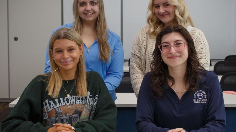 group of four students posing in a classroom for group photo