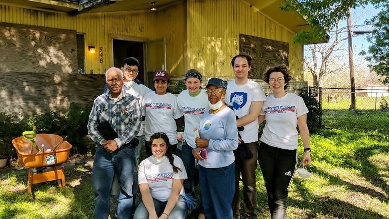 Students stand with homeowners outside a Houston residence damaged by Hurricane Harvey.