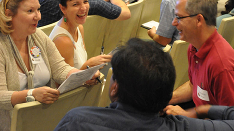 Faculty members sit together discussing and laughing