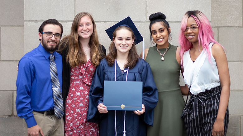 4 students stand with fellow student that's wearing a cap and gown at graduation