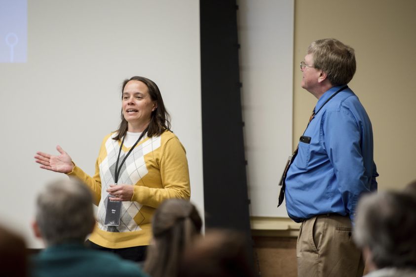 Gina talks while Griff listens and looks toward presentation screen