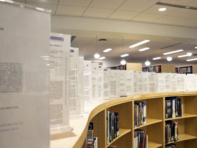 framed copies of faculty members' published works line the top of a display area in the Scranton campus library